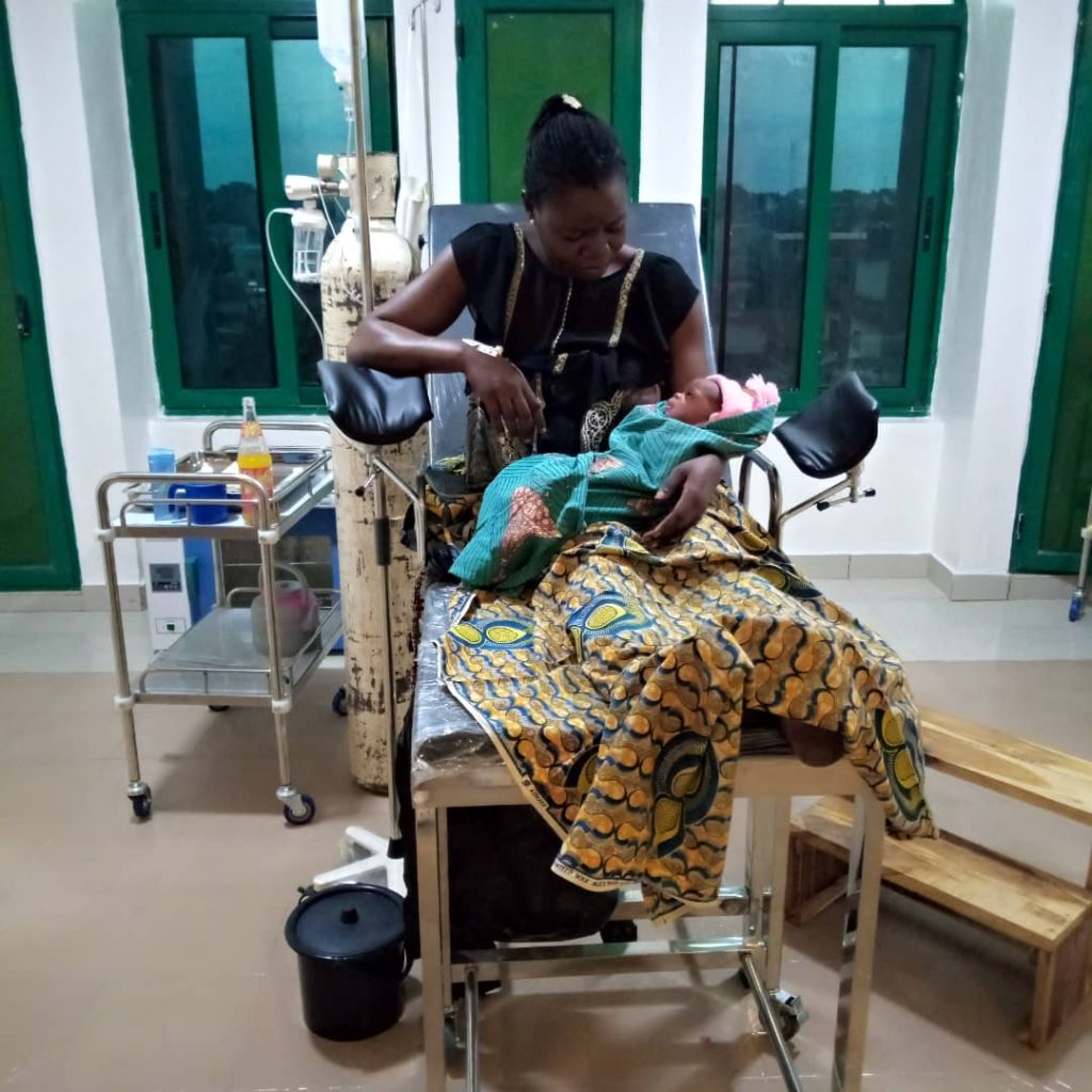 Picture of the first woman to give birth at the Help To Help free clinic in Lome, Togo holding her infant child in the patient room.